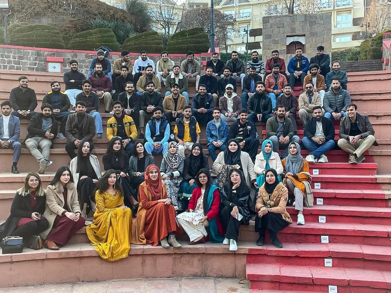 The whole team seated in rows on the red steps of an outdoor amphitheatre