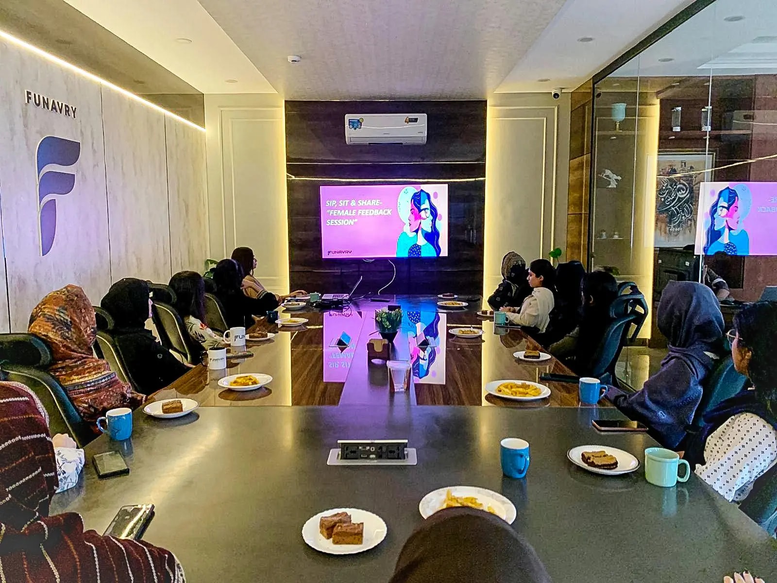 Women of the team seated around the boardroom table for a Sip, Sit & Share feedback session