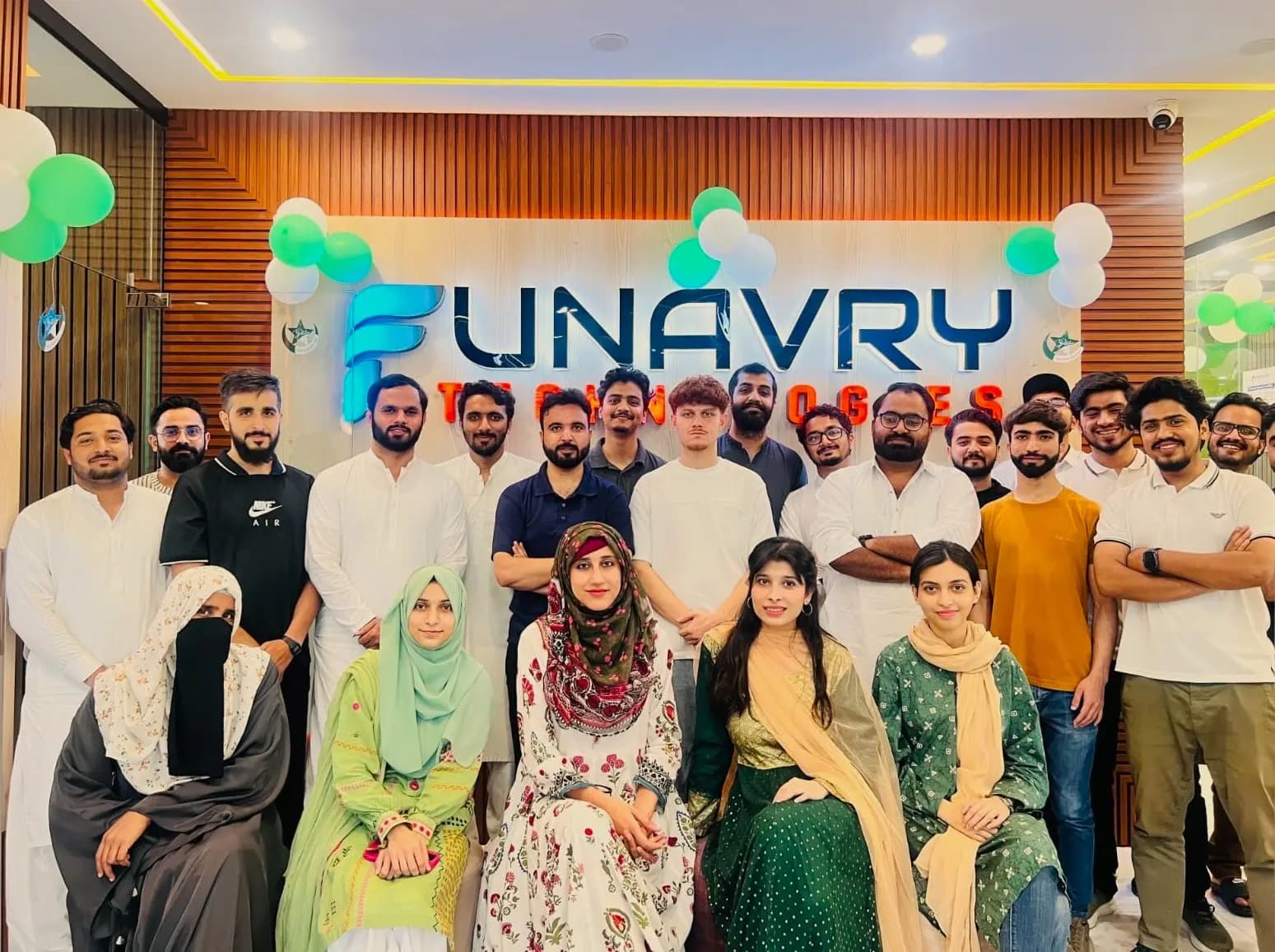 The team gathered in front of the illuminated Funavry Technologies sign, decorated with green and white balloons